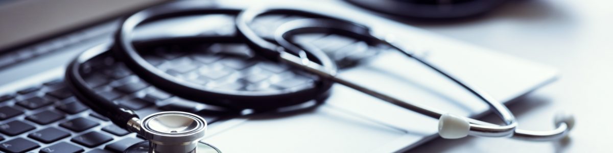 Stethoscope on laptop keyboard in doctor surgery with blood pressure monitor